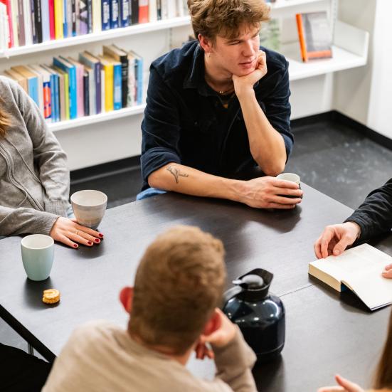 Gruppe omkring et bord, mand med bog. Foto: Christopher Egeberg (Flip)