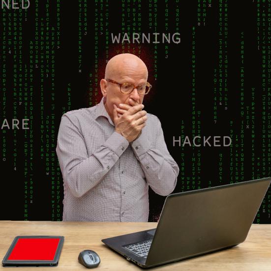 fortvivlet mand der står og ser på sin computer, med ord som "ransomware", "hacked" og "warning" stående rundt om sig.