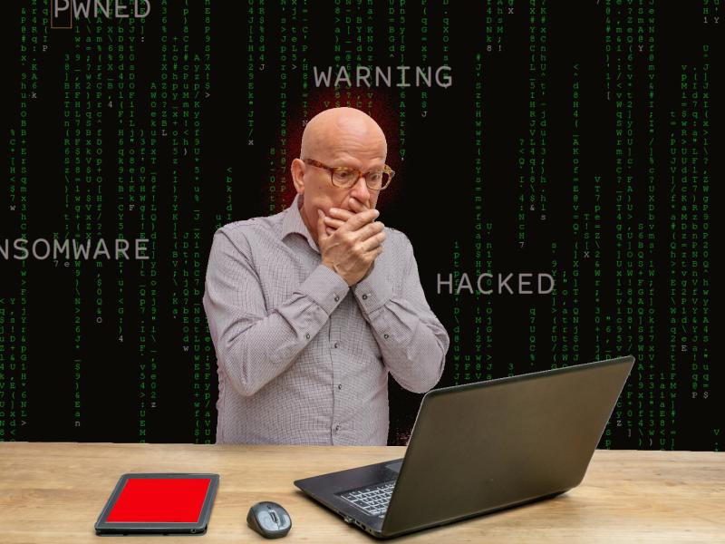 fortvivlet mand der står og ser på sin computer, med ord som "ransomware", "hacked" og "warning" stående rundt om sig.