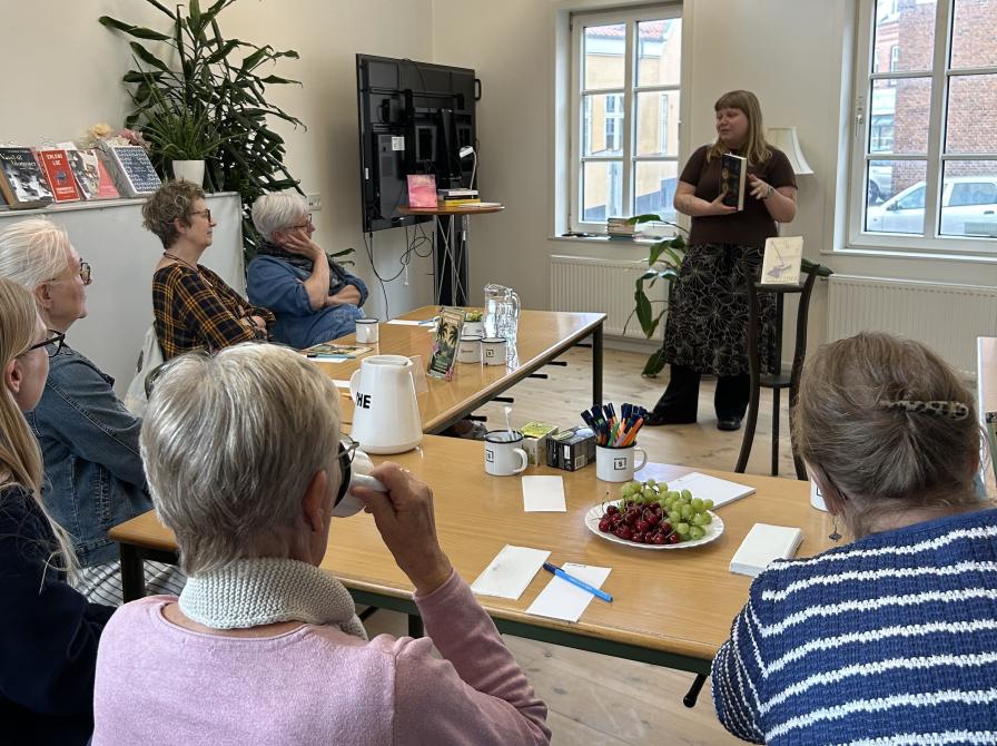 Mathilde holder en bog foran gæster til bogcafé